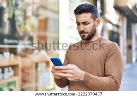 Young hispanic man using smartphone at street