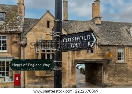Close up of the signage in the middle of Chipping Campden, UK indicating the Heart of England Way and Cotswold Way for hiking with out of focus typical Cotswolds limestone cottage in background