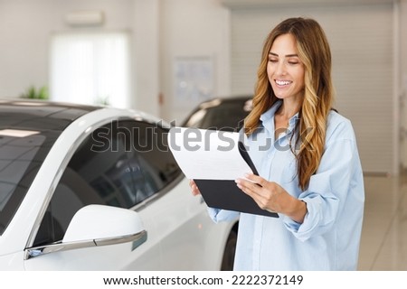 Fun woman 20s customer buyer client in blue shirt hold document reading agreement choose auto want to buy new automobile in car showroom vehicle salon dealership store motor show indoor Sales concept Royalty-Free Stock Photo #2222372149