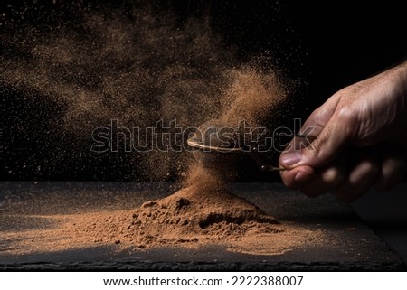A creative photo of cocoa powder on a black background. Hand with cocoa powder through a small sieve. 