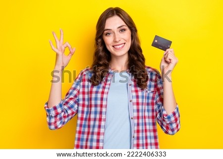 Photo of charming cute girl dressed checkered shirt rising debit card showing okey sign isolated yellow color background