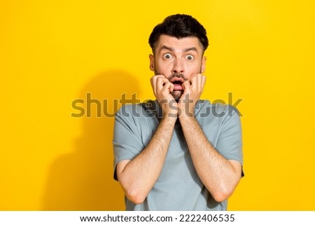 Closeup photo of young excited stressed funny man bearded bite fingers nervous scared watching movie unexpected isolated on yellow color background