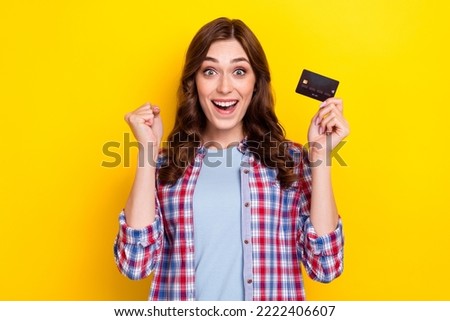 Photo of cute lucky girl dressed checkered shirt rising fist holding debit card isolated yellow color background
