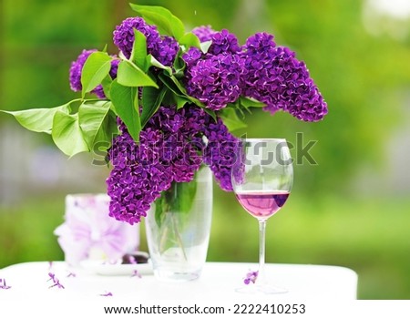              half-empty glass of rose wine and a bright bouquet of lilacs, on a white table on a sunny day in the garden.    background            