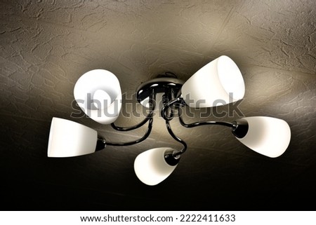 A chandelier made of white plafonds and shiny rods. Beautiful chandelier of five lamps on the ceiling at night. A luminous chandelier. Vintage closeup. Construction decoration concept.