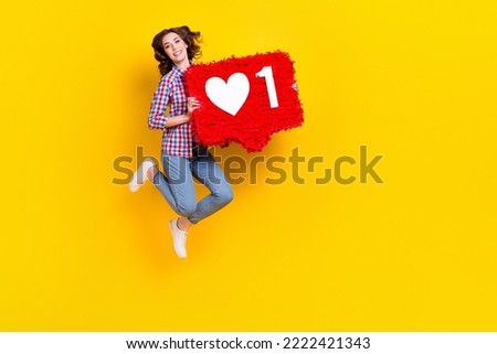 Full length photo of satisfied girl with wavy hairdo checkered shirt hold big red social media like isolated on yellow color background