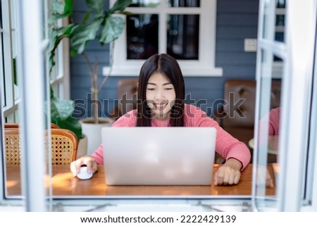 Close-up of smiling Asian woman looking at laptop screen and smiling happily