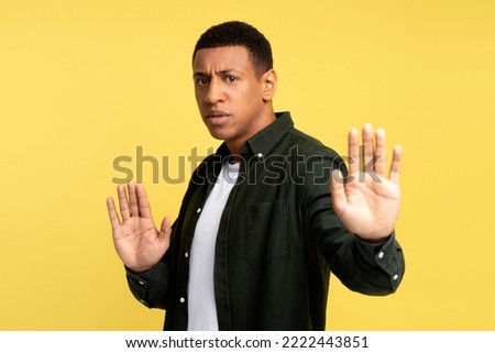 No! Confident young man with serious face showing stop gesture with his palm, teenager against bullying and violence. Indoor studio shot isolated on yellow background 