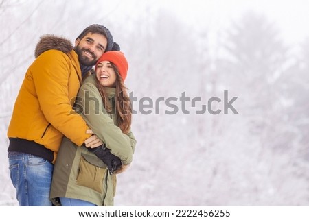Beautiful young couple in love spending winter vacation in the mountains, hugging and relaxing outdoors on snowy winter day