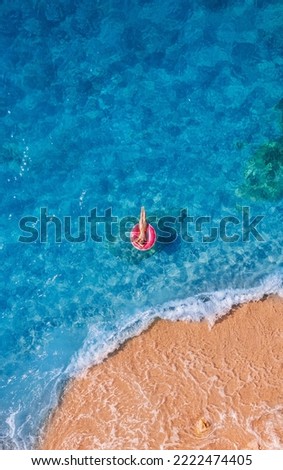 Young woman swimming on pink inflatable donut in turquoise sea with wave, aerial top view. Concept travel beach resort.