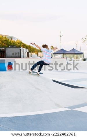 Rear view of hairy skateboarder doing trick on hill in skate park with arms outstretched
