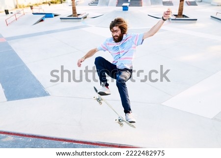 Portrait of bearded tricker jumping on skateboard in park
