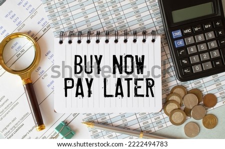 On a white table is a calculator, car key, cash, a pen and a notebook with the inscription BUY NOW - PAY LATER