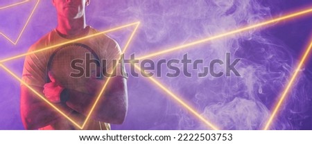 Midsection of caucasian male player holding racket by illuminated triangles on blue background. Copy space, composite, sport, competition, neon, illustration, glowing, smoke and abstract concept.