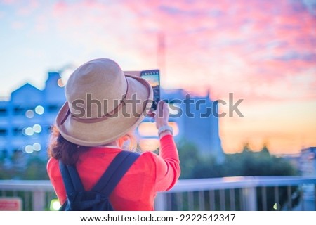 Back view of a woman taking a picture of the sunrise with a smartphone