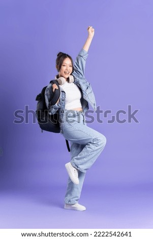 Portrait of a beautiful Asian schoolgirl wearing a backpack on a purple background Royalty-Free Stock Photo #2222542641