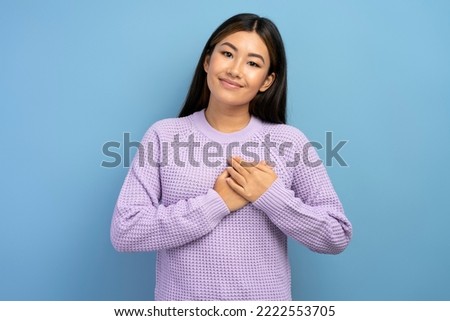 Portrait of sincere honest teen girl in hoodie holding hand on chest, pledging allegiance, taking oath with responsible expression. Indoor studio shot isolated on blue background  Royalty-Free Stock Photo #2222553705