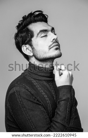Black and white portrait of a handsome man with stylish hair, in a turtle neck sweater style, posing in a studio with eyes closed with a hand near face Royalty-Free Stock Photo #2222610945
