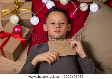 boy showing craft envelope close up.child wrote a letter to santa.christmas letter for santa claus.child holding an envelope with a letter.boy at the christmas tree