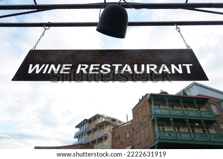 Vintage rusted metal signboard for wine restaurant hanging on iron chains.  historical buildings with wooden balcony and blue sky on background. TBILISI, GEORGIA
