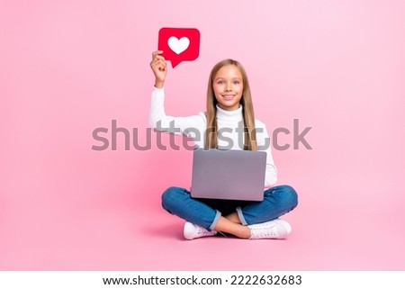 Full size photo of positive schoolkid sit floor arm hold paper like card use netbook isoated on pink color background