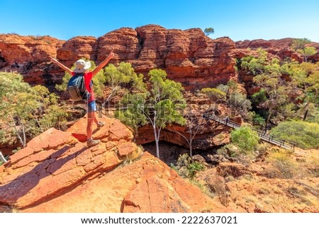 Panoramic view of woman at Kings Canyon Rim Walk with footbridge over Garden of Eden, Watarrka National Park, Australia. Female visitor enjoying scenic views in outback Red Center, Northern Territory. Royalty-Free Stock Photo #2222637021
