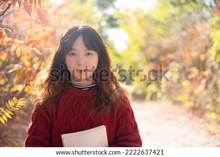 Beautiful Asian women are in the park in autumn. The red leaves in the sun are very beautiful
