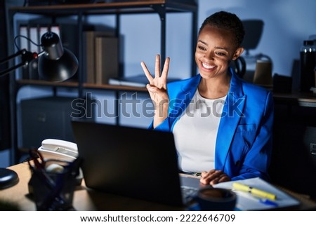 Beautiful african american woman working at the office at night showing and pointing up with fingers number three while smiling confident and happy. 