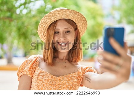 Young redhead woman tourist wearing summer hat make selfie by smartphone at park