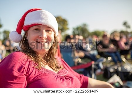 An Australian caucasian woman wearing a Santa hat at out door Christmas carols by candlelight in the summer