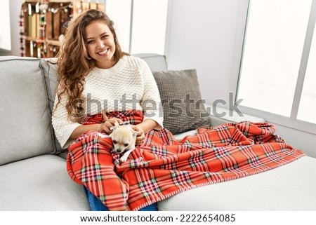 Young beautiful hispanic woman sitting on sofa with dog at home
