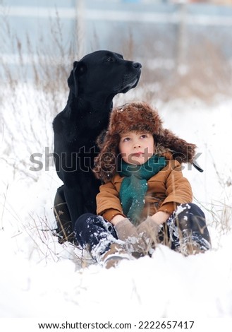               a little boy in the snow with a labrador on a winter walk look into the distance. Human and dog friendship concept. Winter holidays concept. Photo with background blur                 
