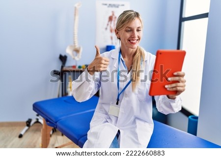 Beautiful woman working at pain recovery clinic doing video call smiling happy and positive, thumb up doing excellent and approval sign 