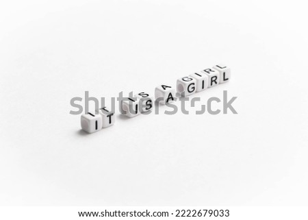 Gender reveal. It is a girl text displayed diagonally on the image. White plastic letter cubes placed on white background.