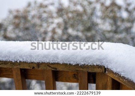 Macro closeup of snow powder covering wooden deck railing in winter with snowing falling snowflakes in Colorado