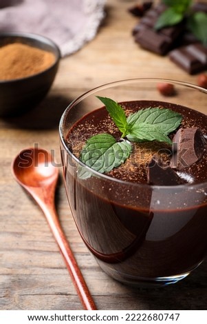 Glass of delicious hot chocolate with fresh mint and spoon on wooden table