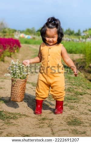 Little girl holding basket in yellow t-shirt smelling flower in the field on the sunset. Baby having fun outdoors. Kid exploring nature. Farming concept,harvesting wallpaper.