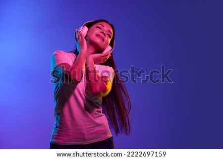 Lovely sounds. Closeup young girl, student in white headphones isolated on blue and pink color background in neon light. Concept of beauty, art, fashion, youth, sales and ad, education, studying.