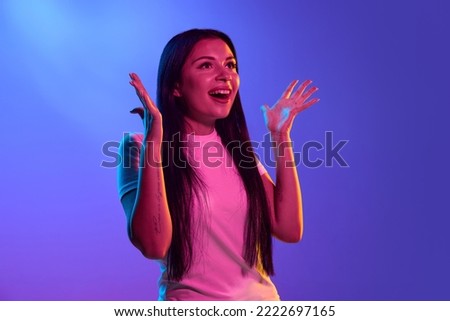 Wow. Portrait of surprised happy pretty young girl, student isolated on dark background in pink neon light. Concept of beauty, art, fashion, youth, sales and ad, education, studying, good news.