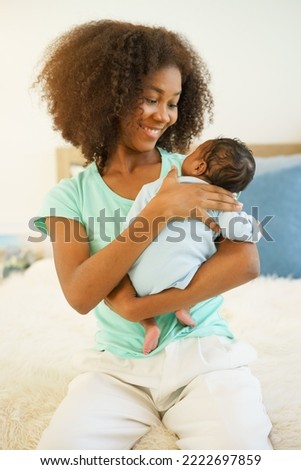 Young mother African American holding her one-month-old newborn baby son carefully and gently in bedroom. Elder sister parenting and playing with adorable little brother infant. Happy mother's day Royalty-Free Stock Photo #2222697859