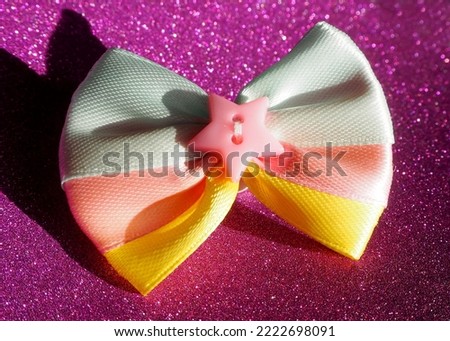 a blue and pink yellow bow with a pink star in the middle lies on a pink shiny background . side view. for top dog notes. accessories