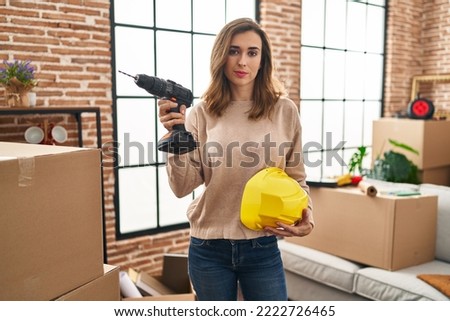 Young woman holding drill at new home relaxed with serious expression on face. simple and natural looking at the camera. 