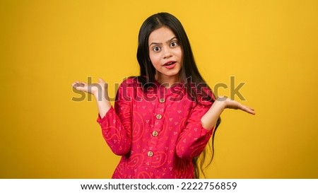 Young Indian girl showing surprised emotion, wearing red Indian dress isolated over yellow background