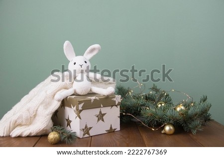 Christmas decoration. Gift box with knitting white rabbit, fir branches on wooden.