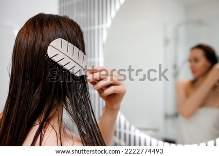 Attractive woman in white towel with comb brushing her wet hair after showering at home in front of bathroom mirror. Cares about healthy and clean hair. Beauty concept Royalty-Free Stock Photo #2222774493