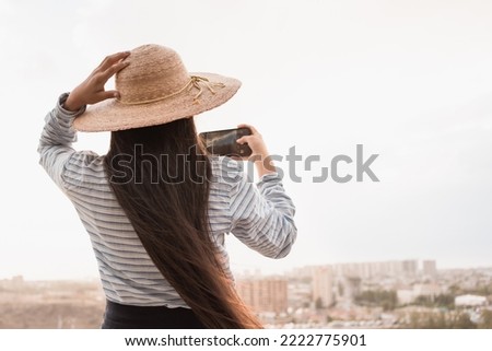 unrecognizable woman in hat standing in city view point and using mobile phone for making video at summer