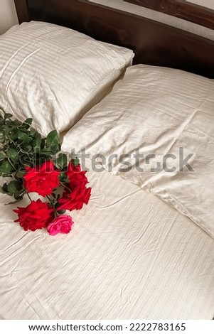 A bouquet of scarlet garden roses lies on the light white satin bed linen. Good morning greeting card.