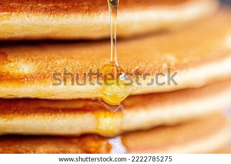 A drop of honey spreads over the pancake.Pancakes with syrup macro shot.Syrup pours on a pancake macro photo.Honey spreads.Drop of syrup close-up.Golden pancakes with glitter syrup.Delicious sweet  Royalty-Free Stock Photo #2222785275