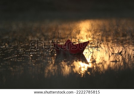 Red paper boat floating in water sunset time golden light creating bokeh effect