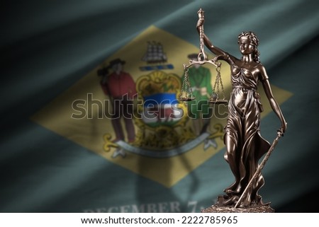 Delaware US state flag with statue of lady justice and judicial scales in dark room. Concept of judgement and punishment, background for jury topics Royalty-Free Stock Photo #2222785965